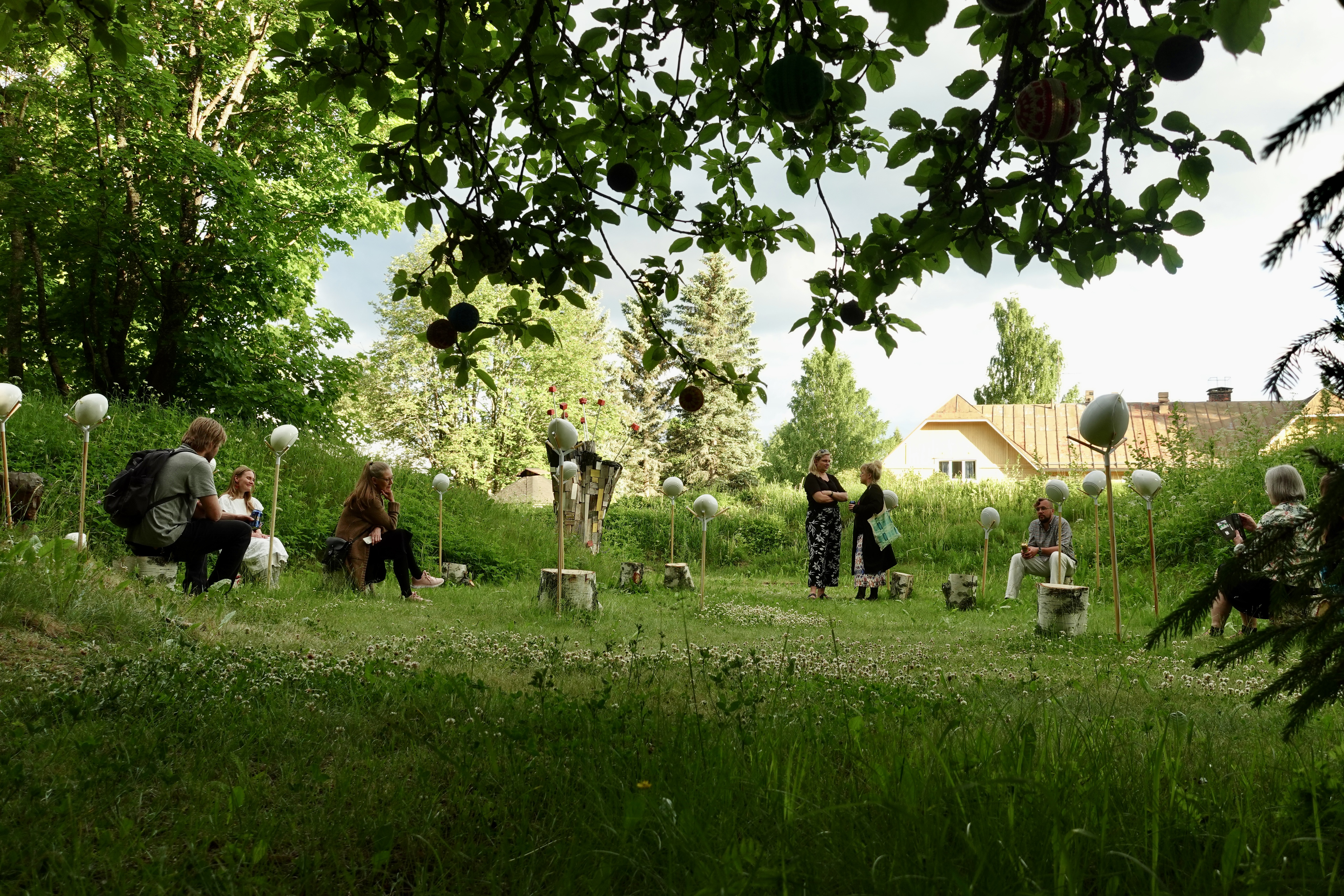 Audience sitting peacefully in the summer grass at Haihatus installation