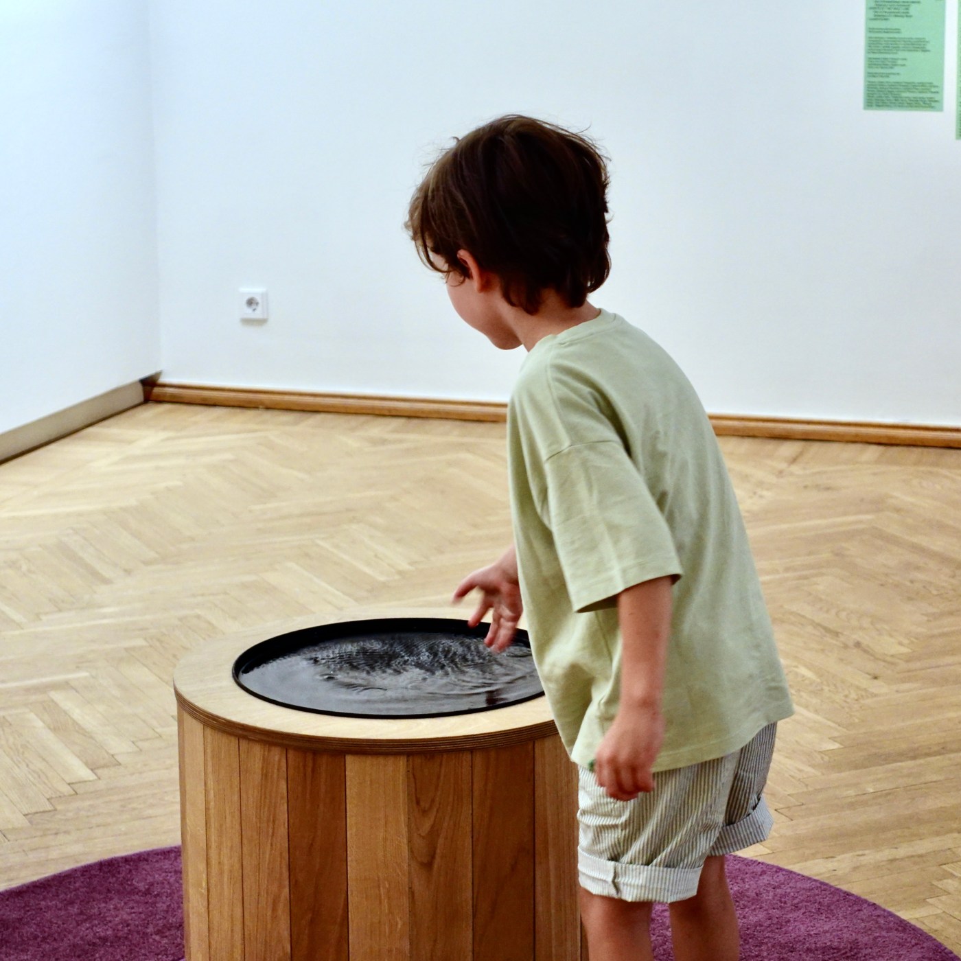 A boy rests his hand on the edge of the well and looks into the water.