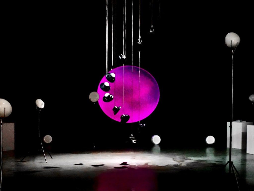 RE-BIRTH: suspended speakers in front of a pink circular projection.