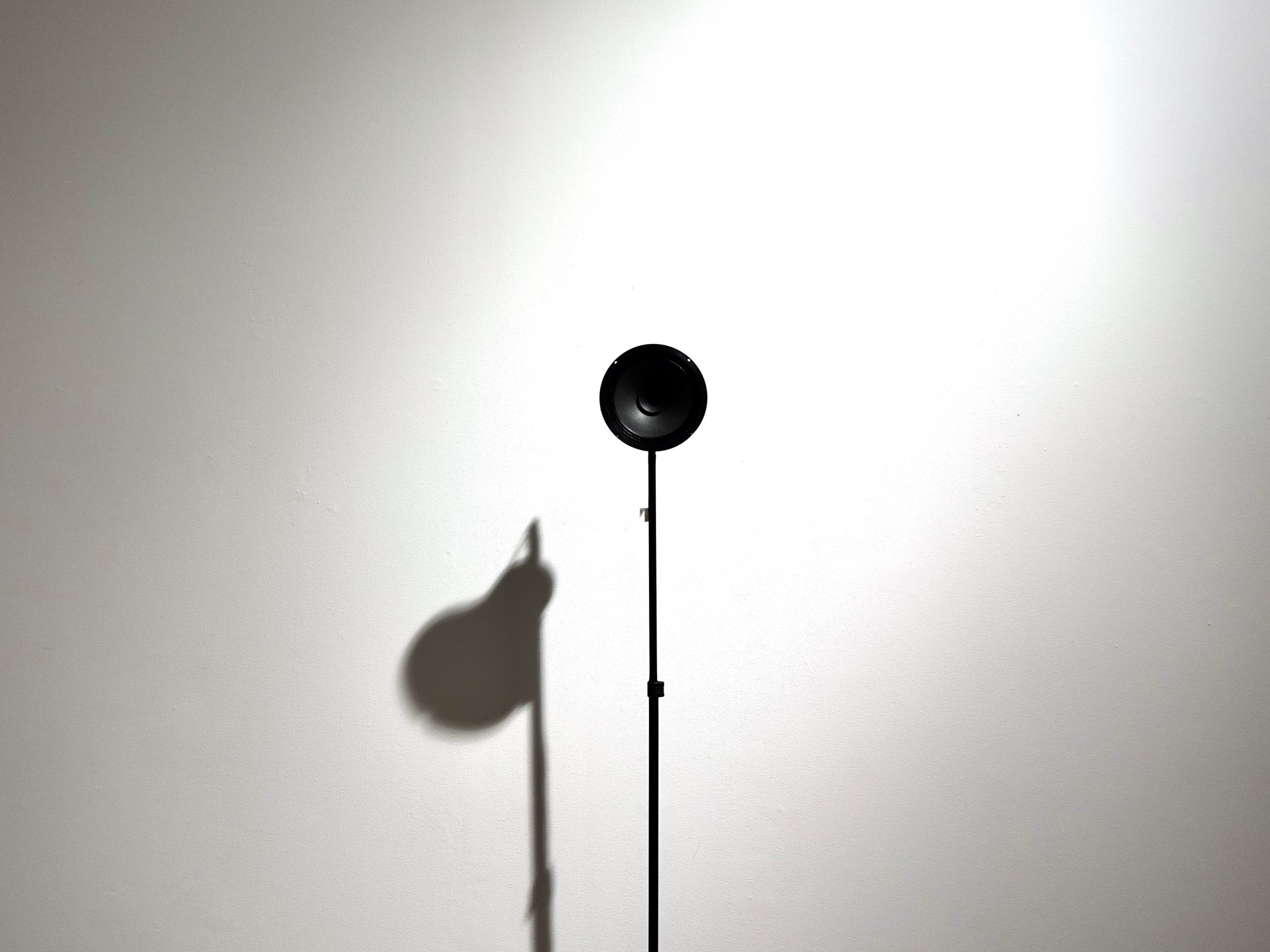 Speaker on a stand casting a shadow against a white wall