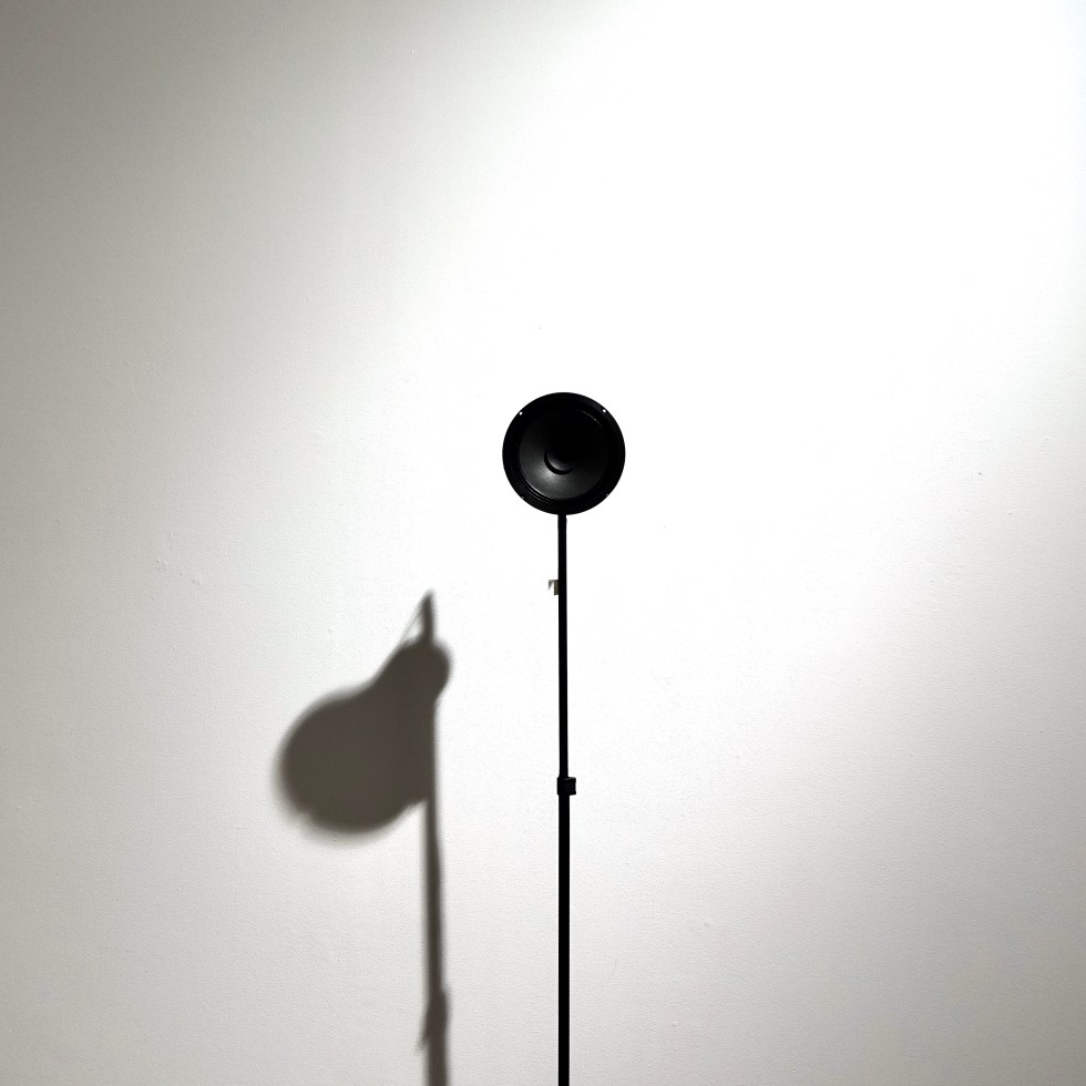 Speaker on a stand casting a shadow against a white wall