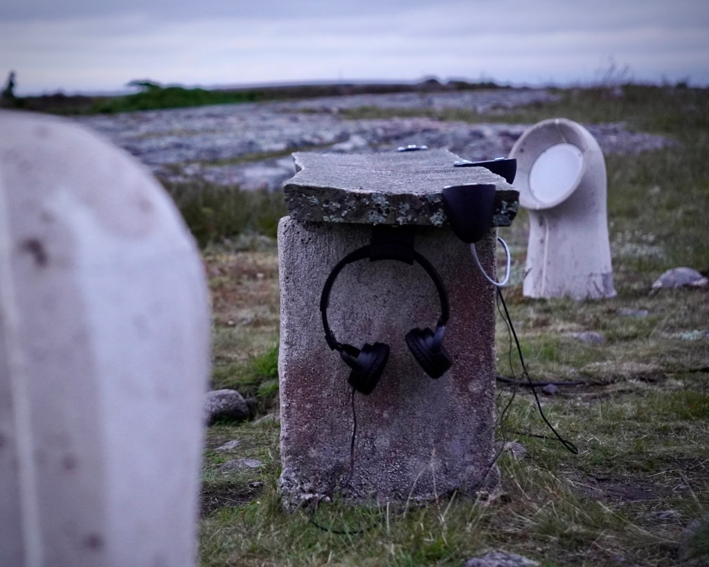 The listening bench of INTER, Jurmo with headphones, among concrete speakers on the island.