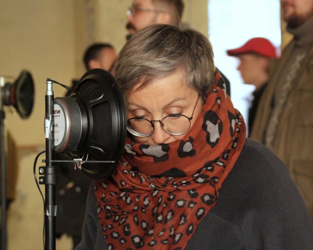 A visitor leaning her head close to a single loudspeaker to hear one voice.
