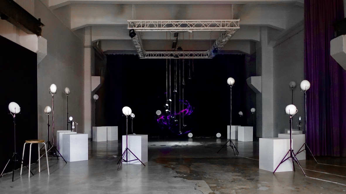 RE-BIRTH in the hall at MUU Helsinki: white breath speakers on stands and plinths lead towards the suspended speaker column and projection.