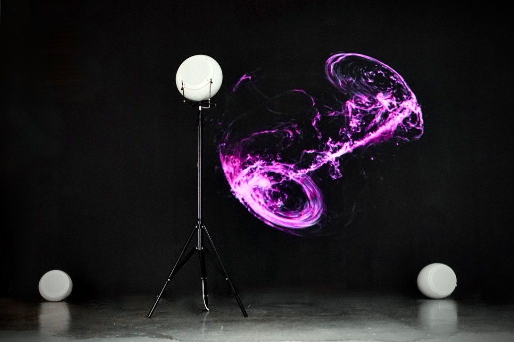 The generative image NIMITTA in purple on a black wall beside a white breath speaker on a stand.